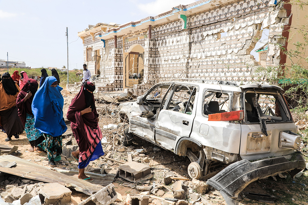 Women walk through the rubble of a car bombing next to a building.