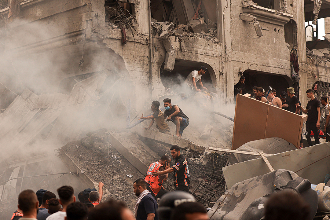 Civilians stand in the rubble of a demolished building.