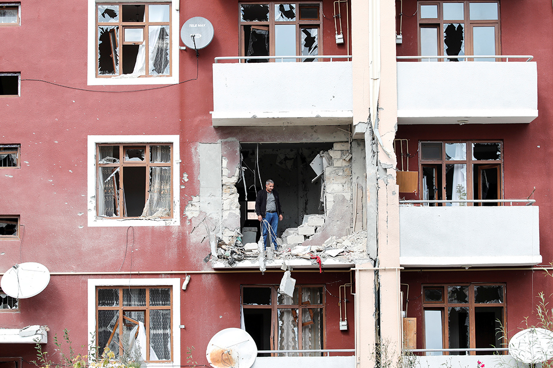 A man stands in a a damaged red apartment building.
