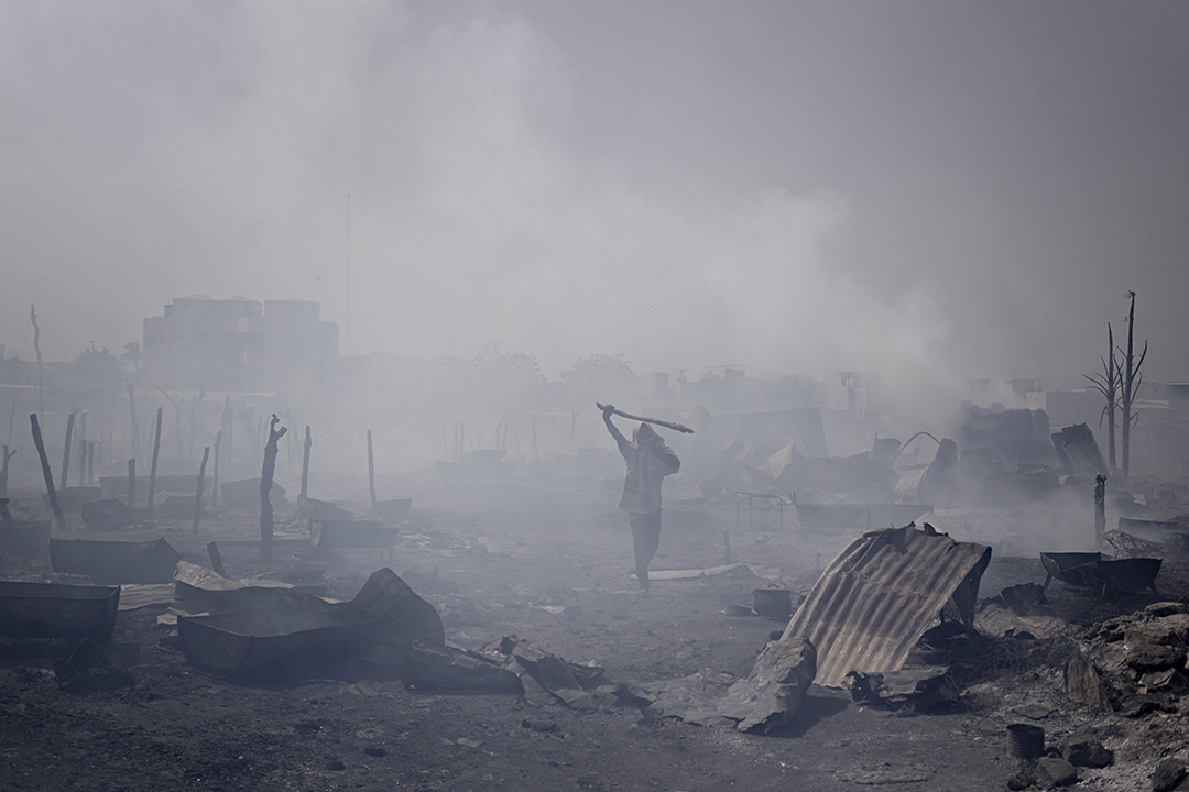 A man walks through a burned out village full of smoke.