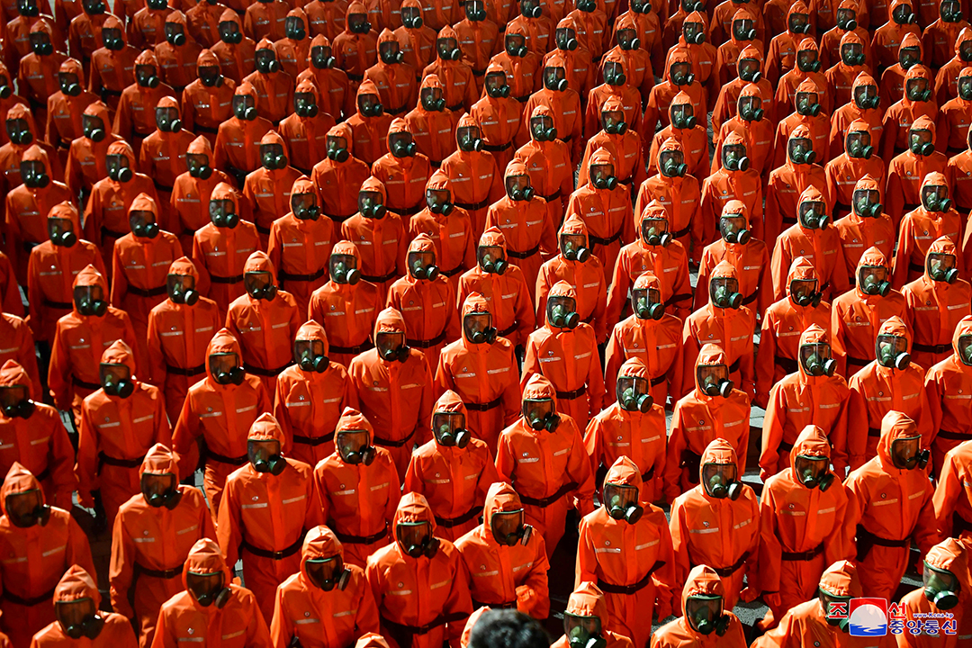 Tens of people stand next to each other in orange hazmat suits. 