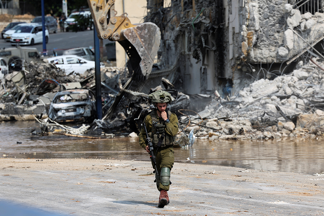 A soldier in green fatigues walks away from a damaged building.