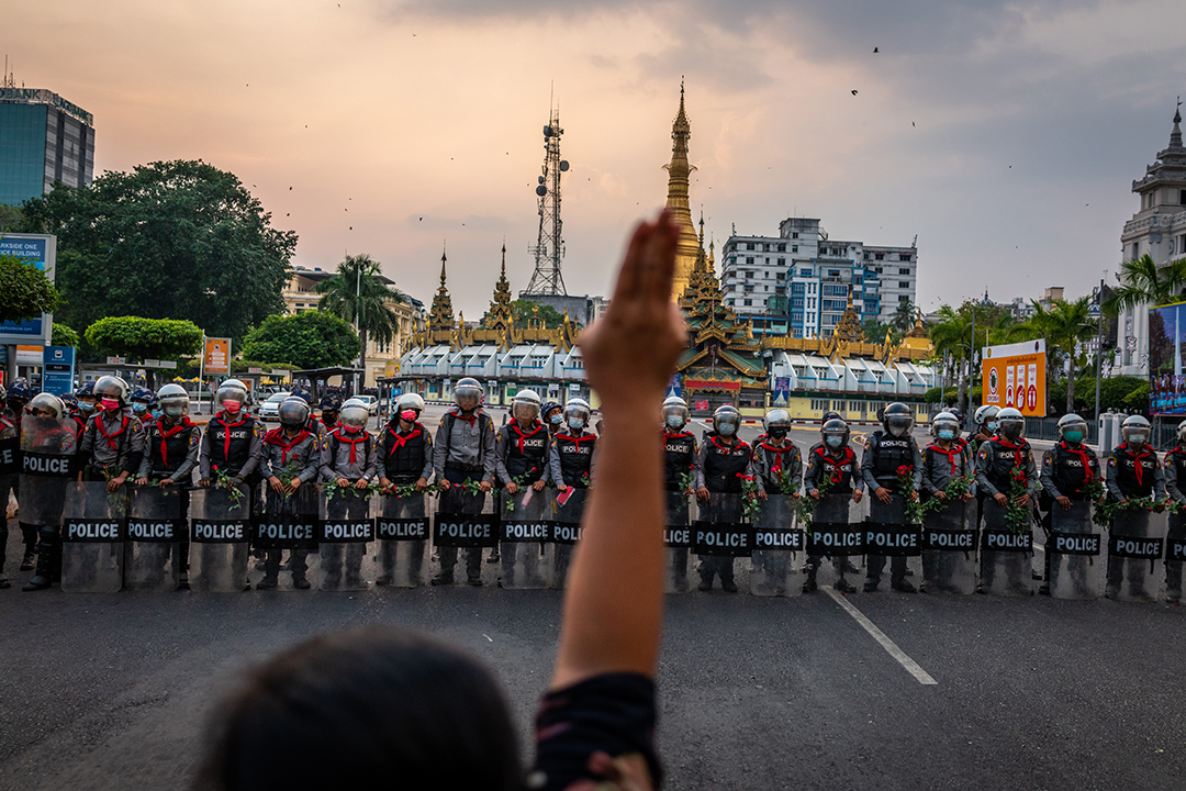 A protester makes a three-finger salute in front of a row of riot police, who are holding roses given to them by protesters
