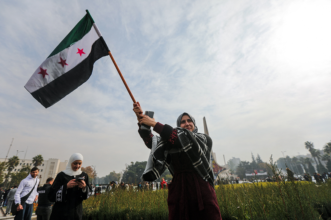 A woman wearing a head covering waves a flag outside.