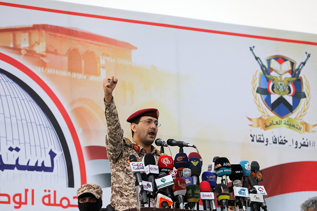 A man wearing military fatigues and a red beret pumps his first in the air while standing at a podium.