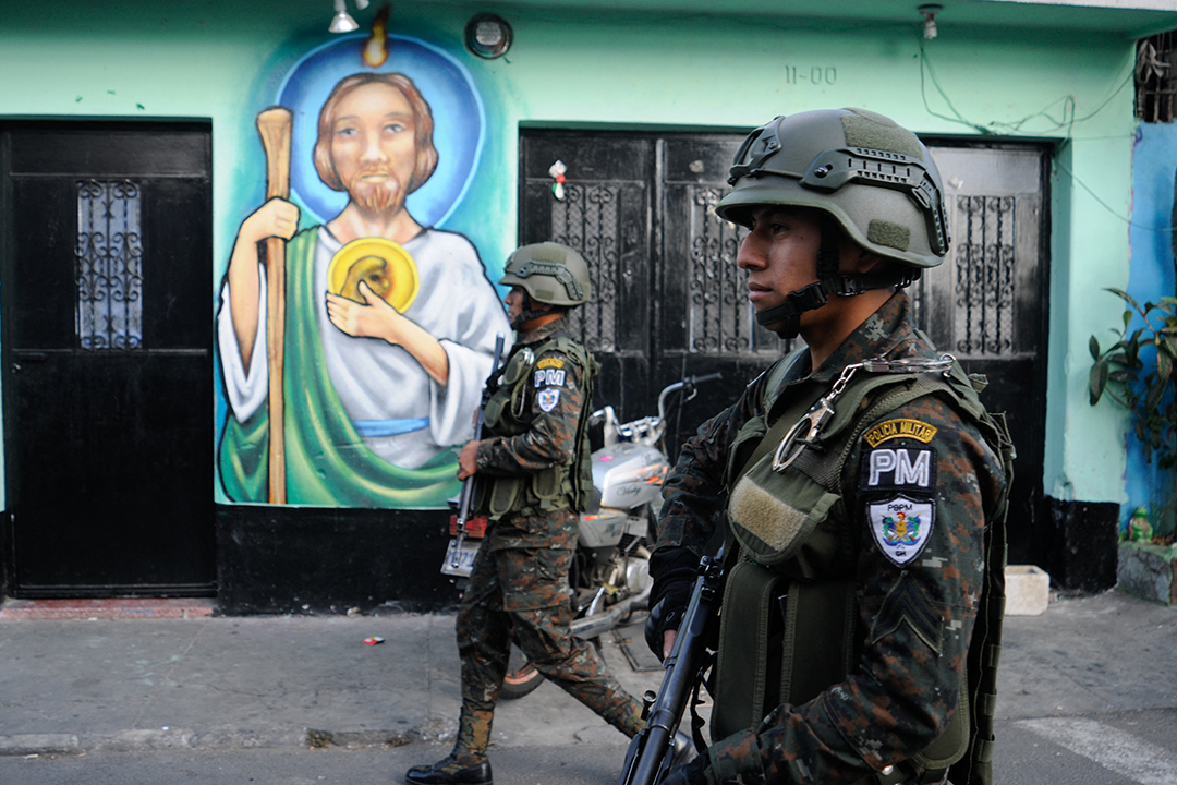 Two soldiers in army fatigues walk beside a building with a mural of Jesus Christ.