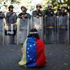 Girl wearing Venezuelan flag sits in front of security forces.