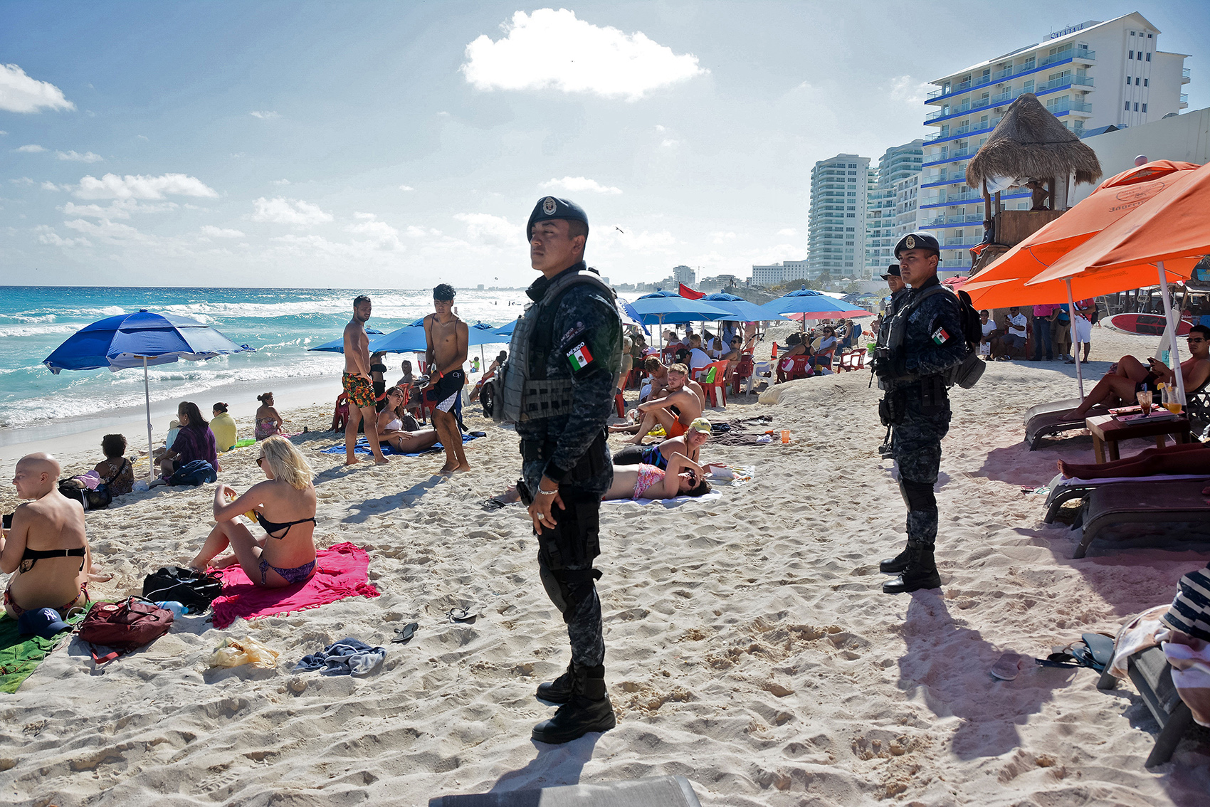 Two police officers stand on a beach flanked by tourists bathing.