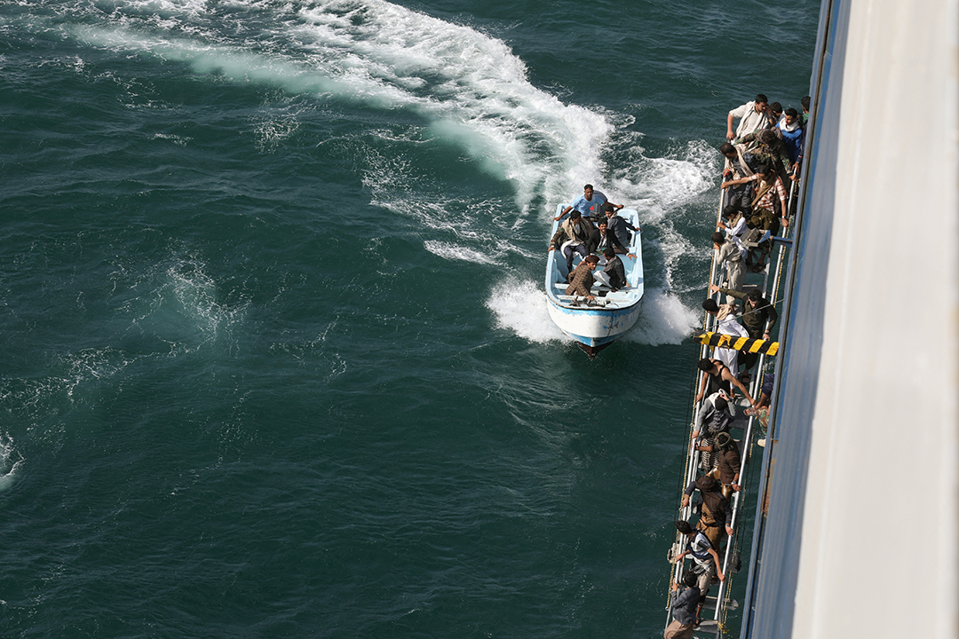 People in a life raft and on the side of a boat in a green sea. 