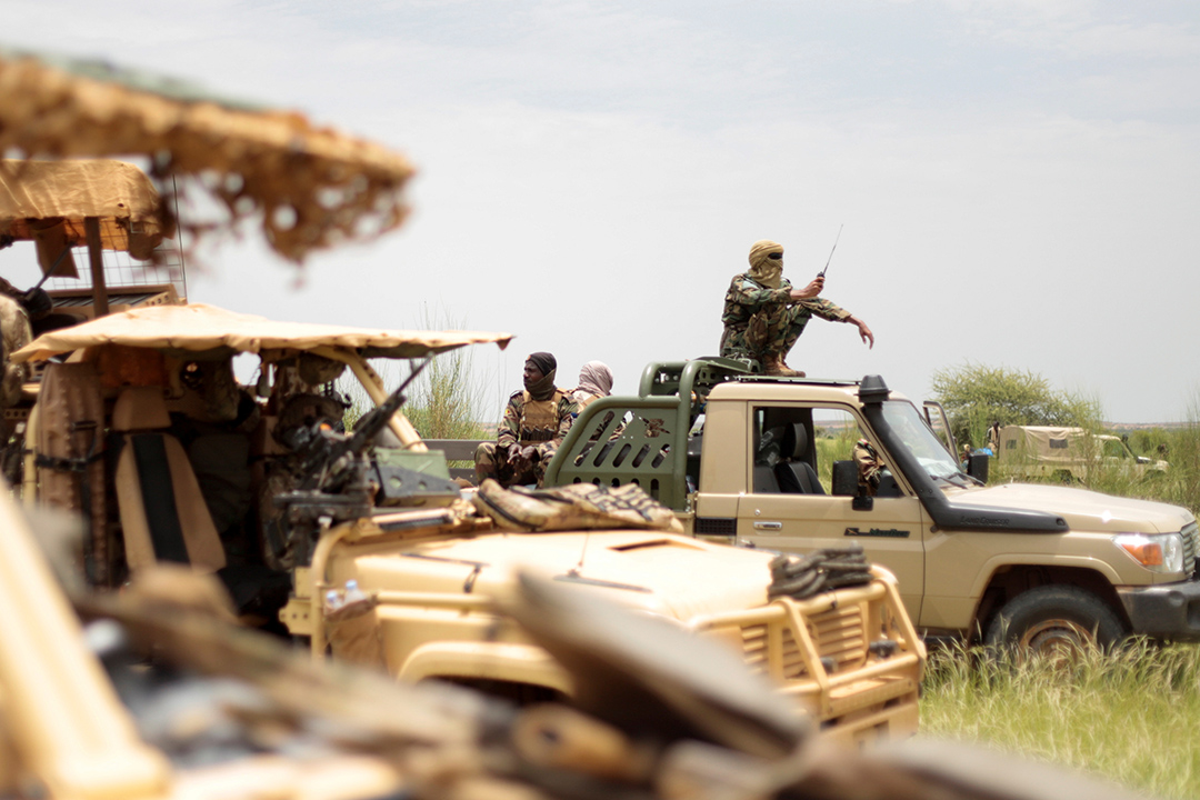 Soldiers stand up inside military vehicles on a grassy plain.