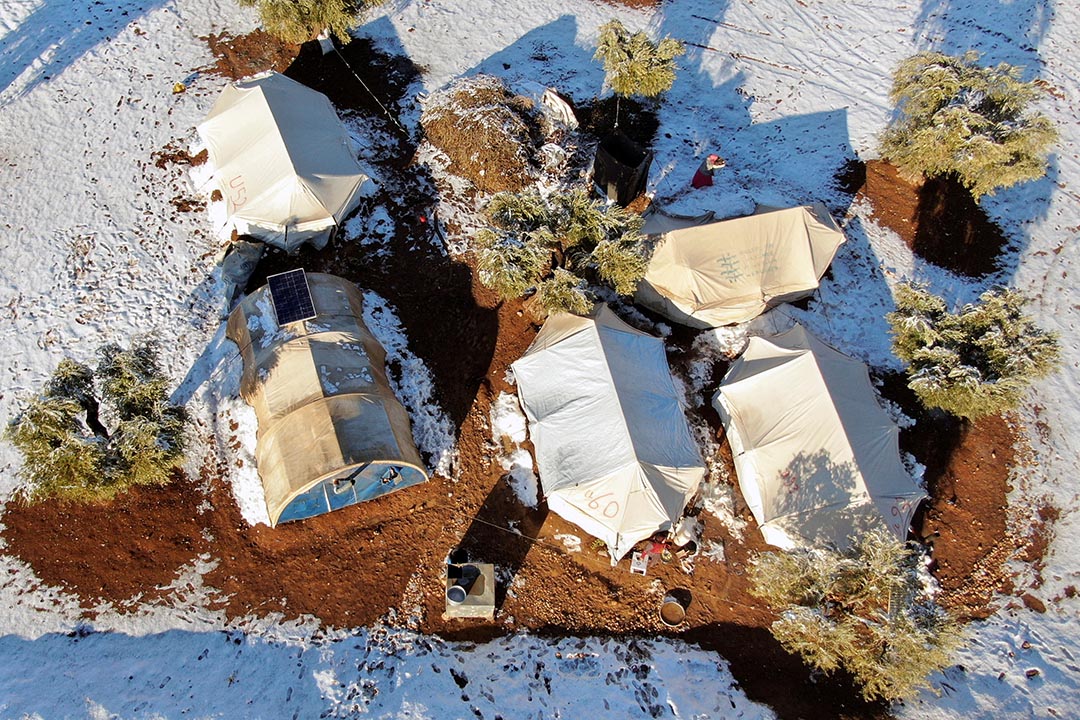 Aerial photo of beige tents partially covered by snow.