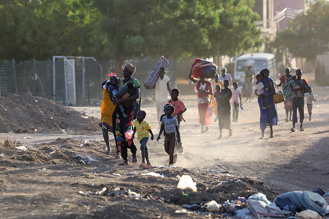 A group of women and children walk through a burned out street carrying their belongings.