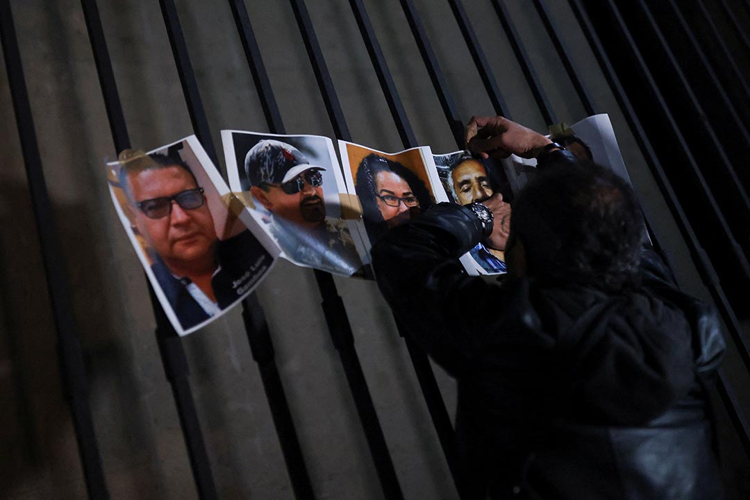 A person faces away from a camera while placing photos of people against a dark wall.