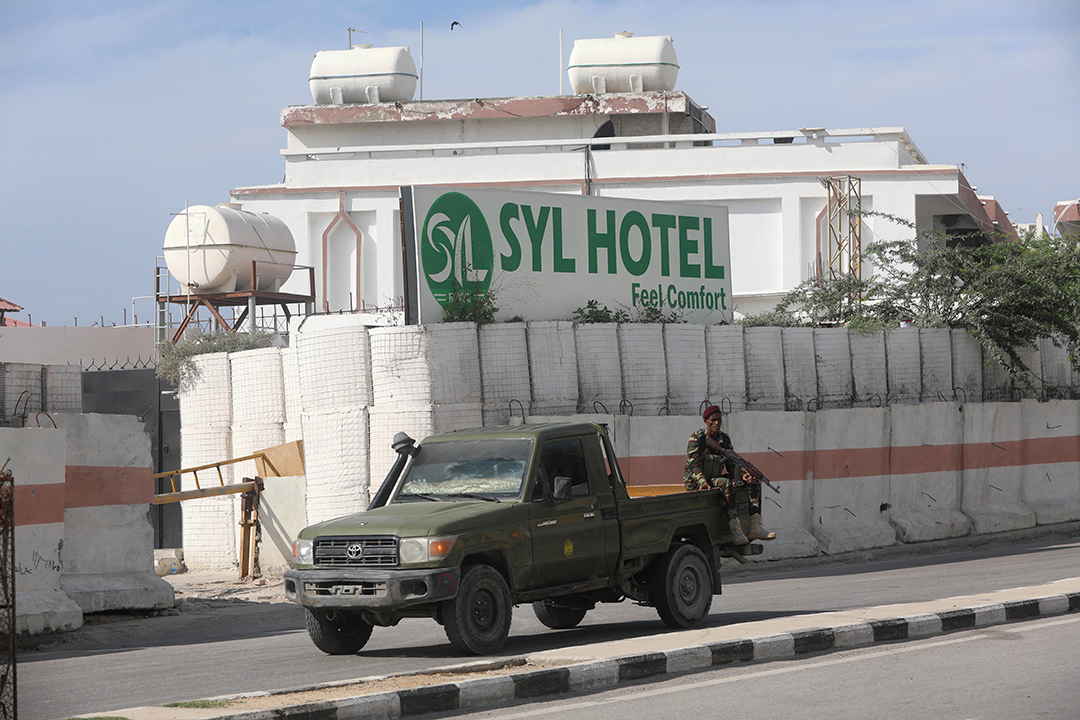 A white hotel building surrounded by concrete walls is guarded by a blue pickup truck.