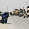 Woman in burqa walking next to tanks.