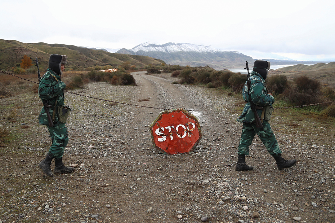 Two soldiers stand by a stop sign in a mountainous terrain.