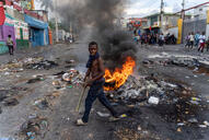 A young man walks past a burning barricade on a street.