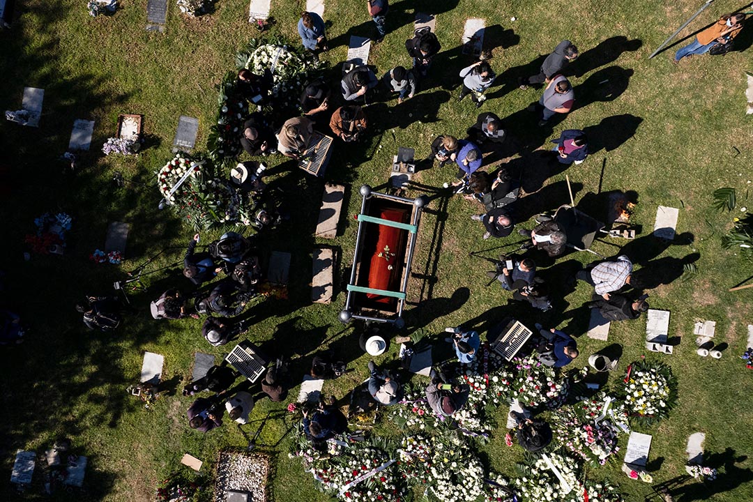 People dressed in black standing on grass gather around a wooden casket in the ground.