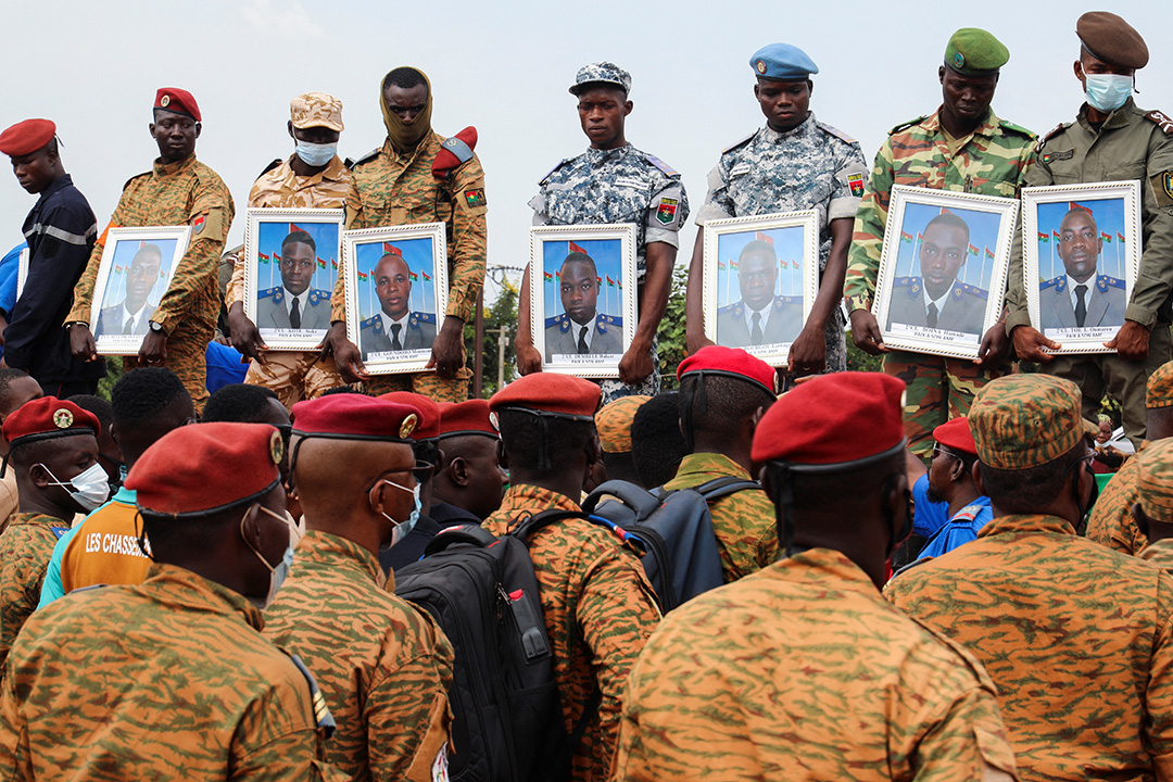 A row of soldiers stand holding portraits of killed soldiers during their funeral.