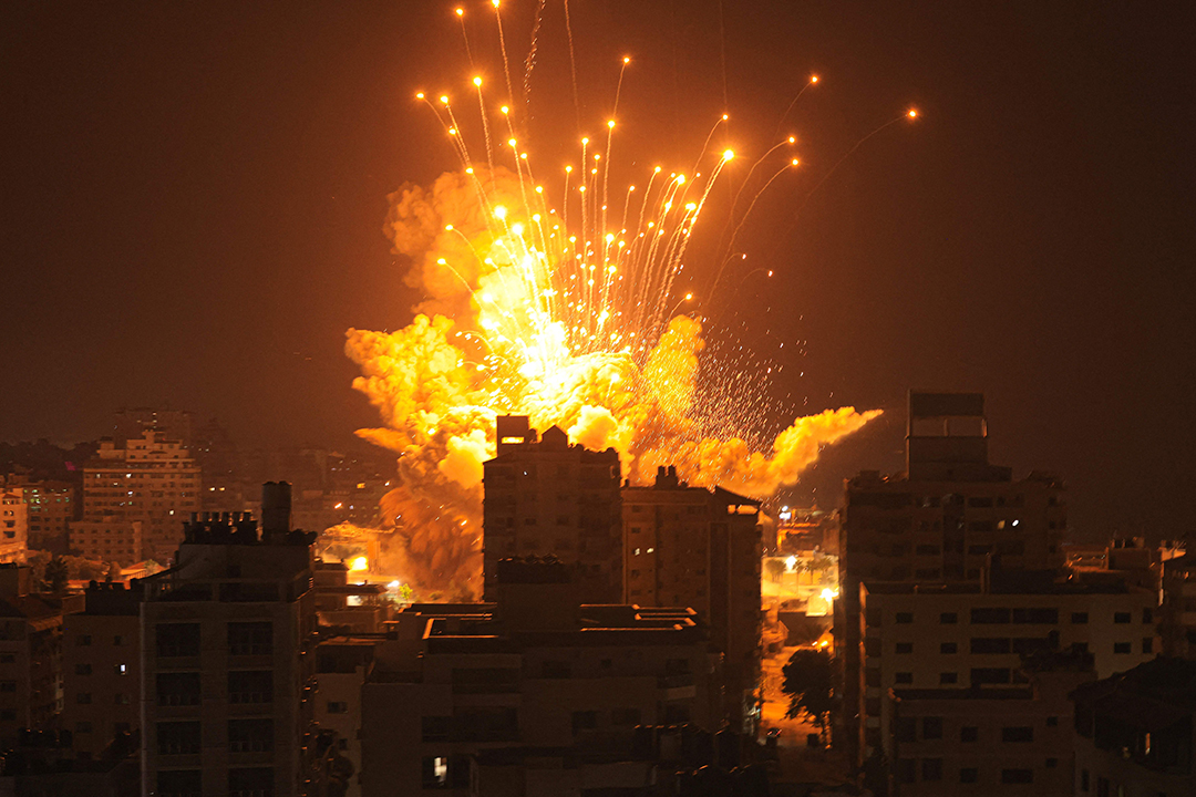A missile explodes in the sky over a building at night.