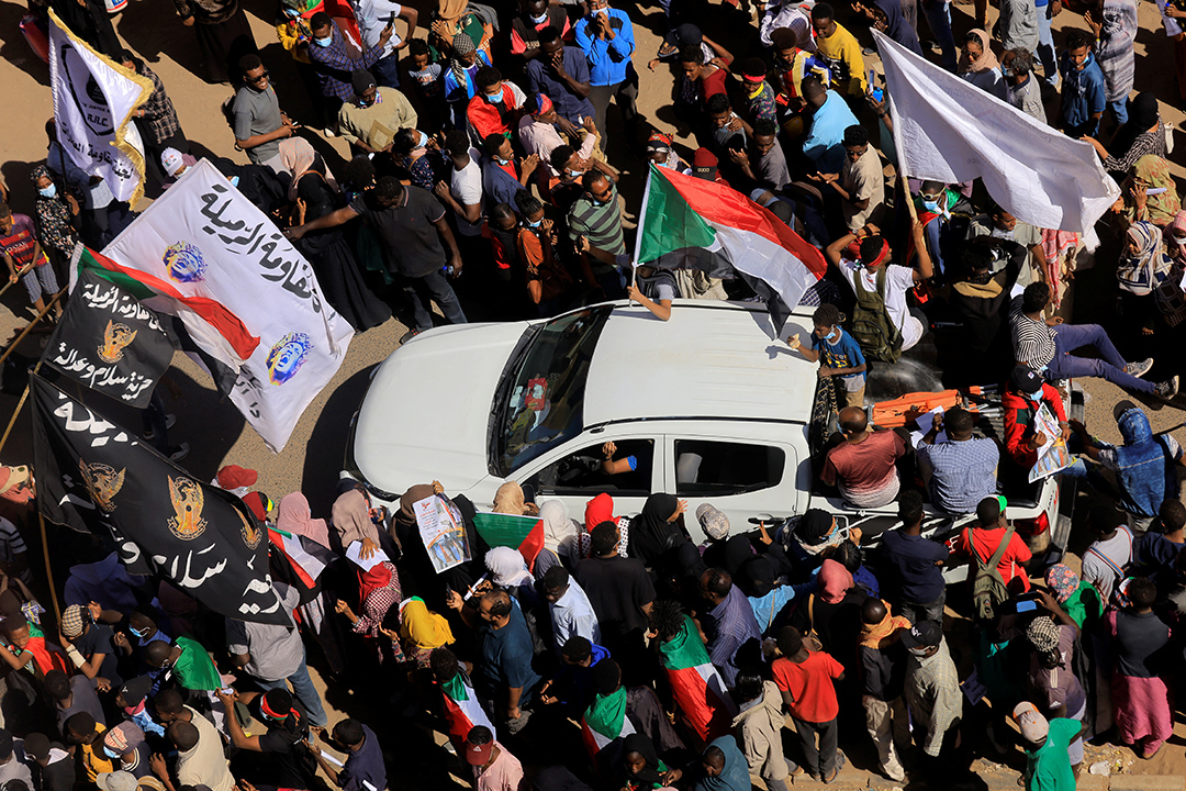 Protestors surround a white car while waving flags.