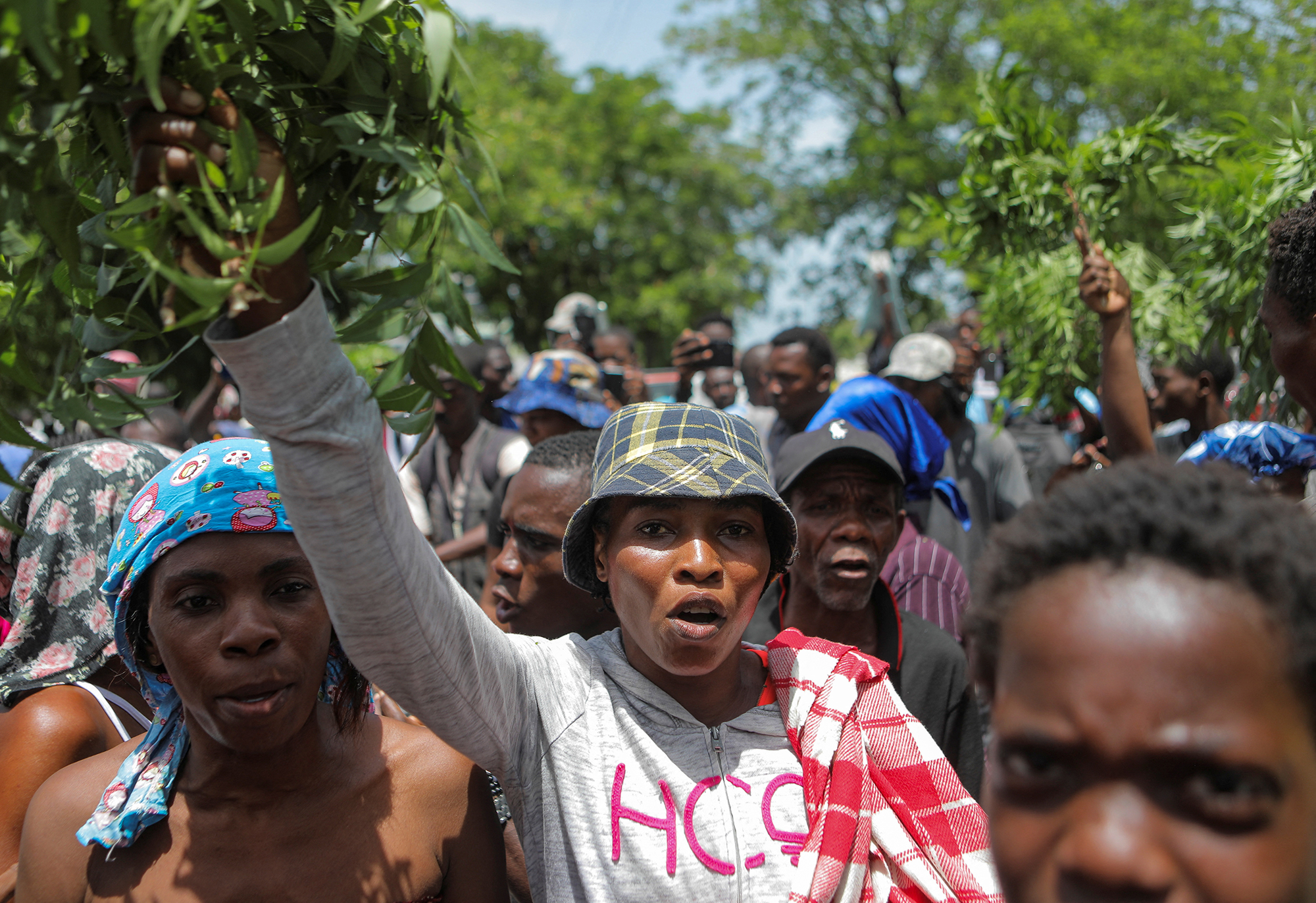 Men and women stand in a group holding green branches over their head as they protest.